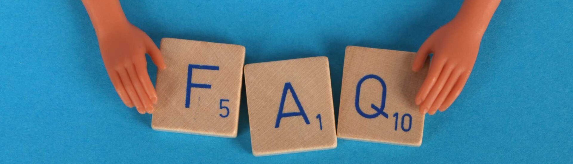 FAQ spelled out with Scrabble tiles held by plastic toy hands on a blue background