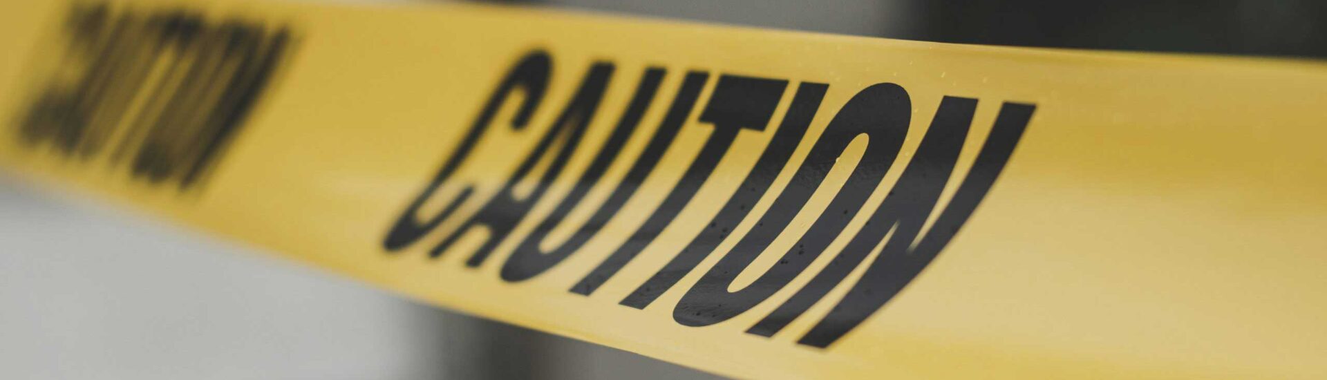 Close-up of yellow caution tape stretched across a blurred background