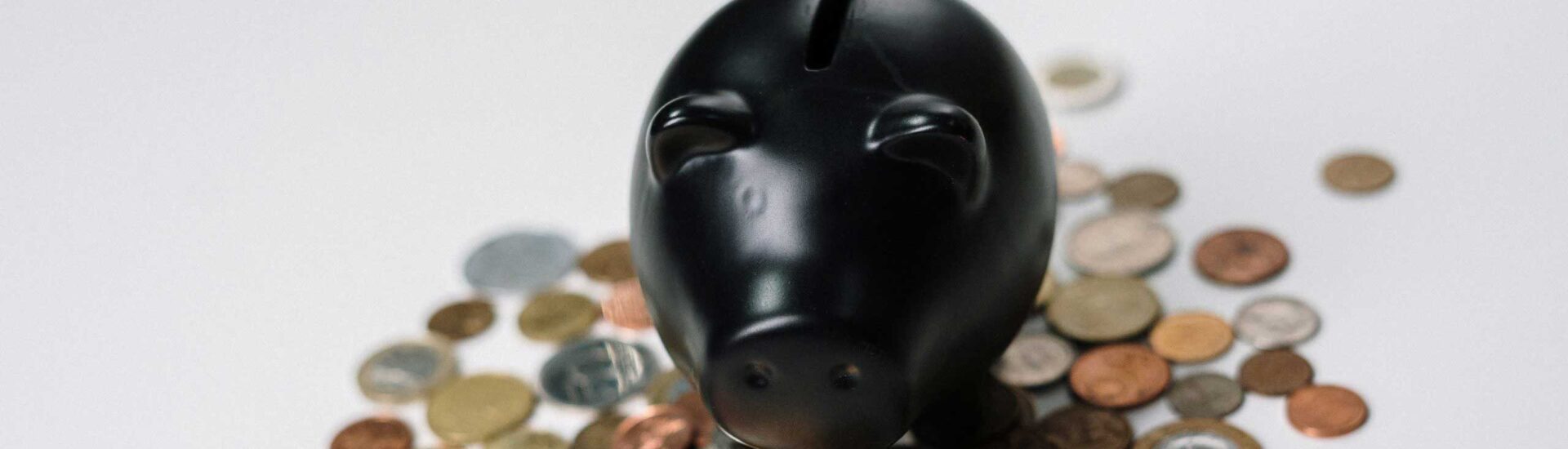 Black piggy bank surrounded by assorted coins on a white background
