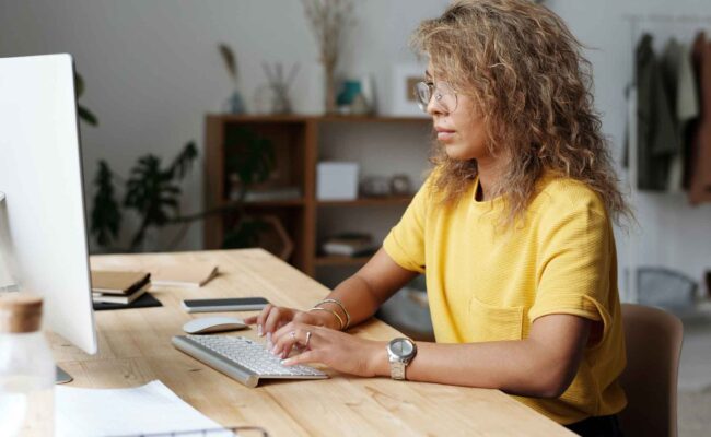 Focused woman in yellow shirt working at a computer in a home office
