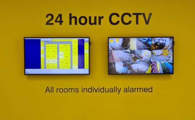 CCTV surveillance monitors on a yellow wall with security alerts